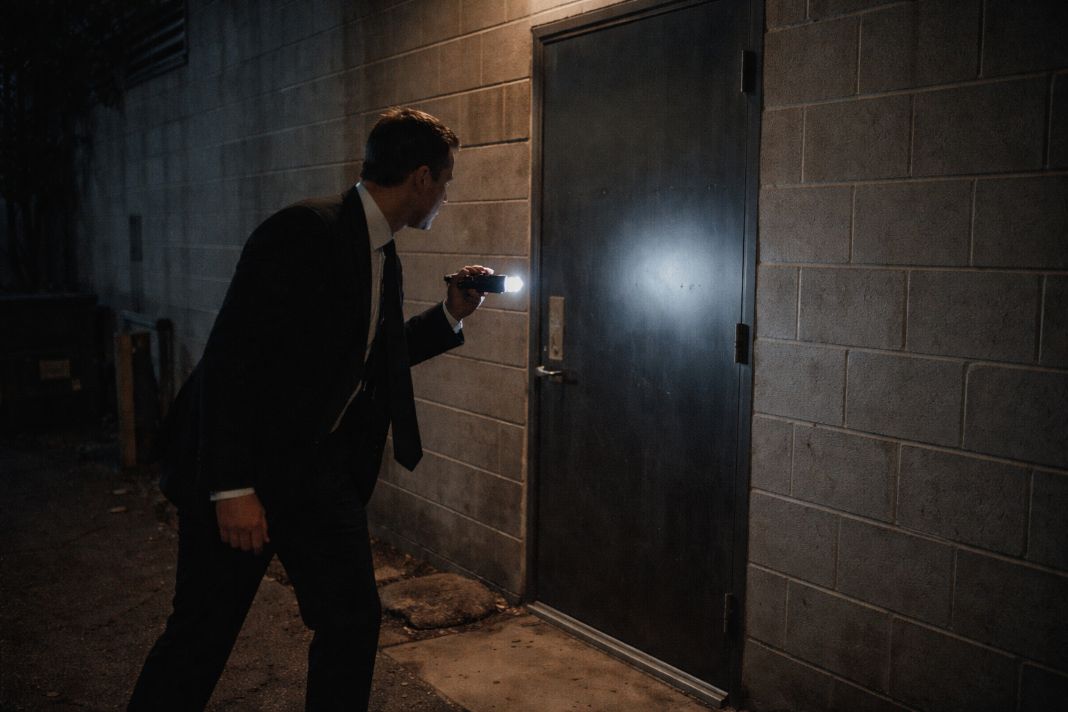 A representative image of a security guard inspecting a dimly lit rear entrance behind an office building
