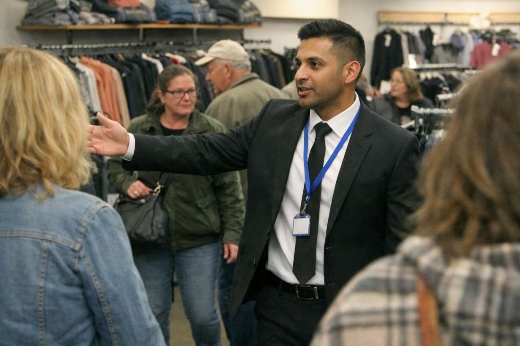 A representative image of security guiding people through a narrow indoor retail clothing aisle ensuring safe spacing