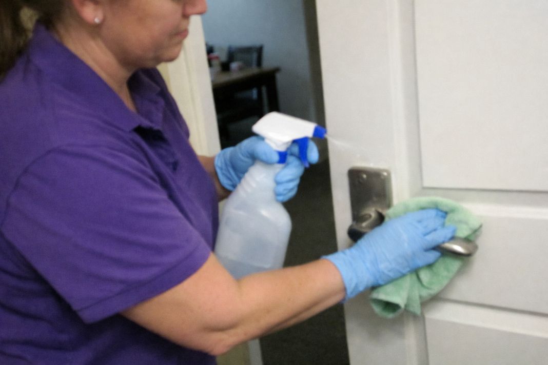A representative photo of an cleaner in a purple polo t shirt and appropriate gloves cleaning a high-touch surface with disinfectant