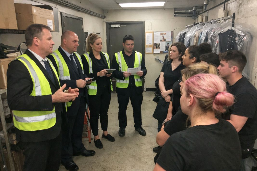 A representative image of a small team in black suits and reflective vests holding a briefing with clothing store staff in a back corridor