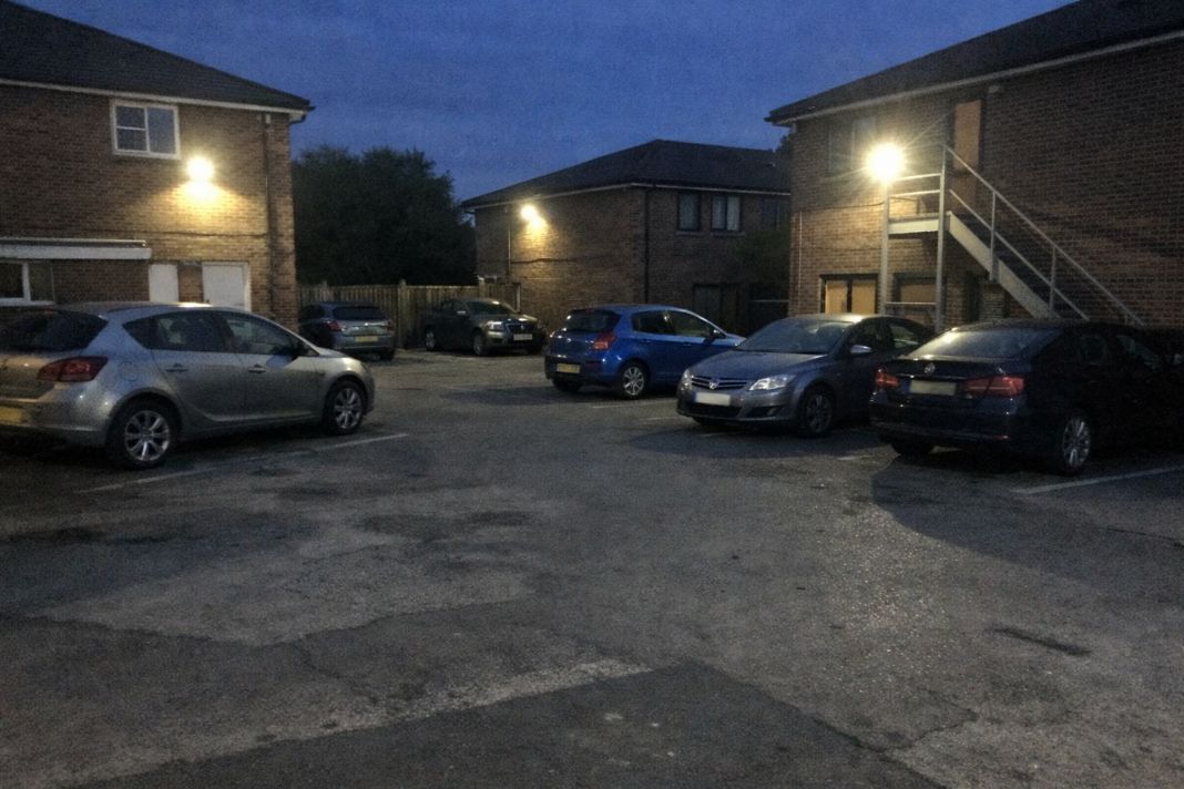 An illustrative image of a business car park in the early evening with visible security lighting