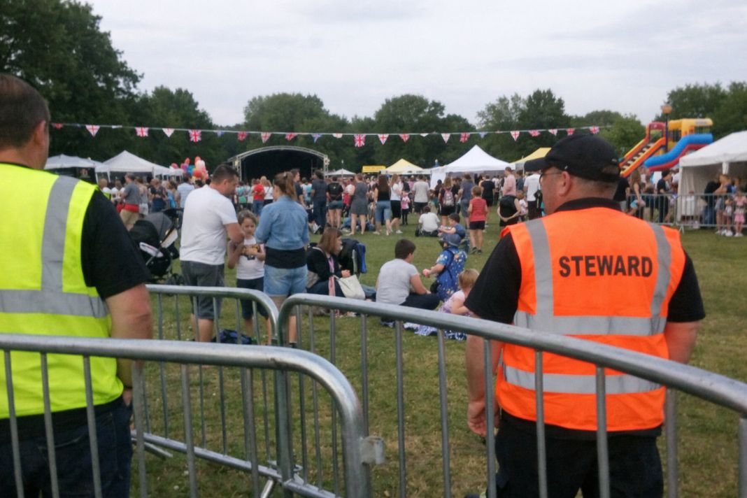 An illustrative image of a UK outdoor event in progress, showing crowd management barriers, stewards