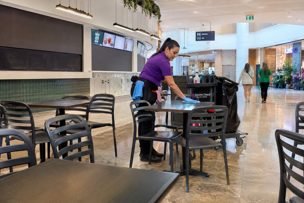 A photo of a cleaner cleaning tables in a shopping centre food hall