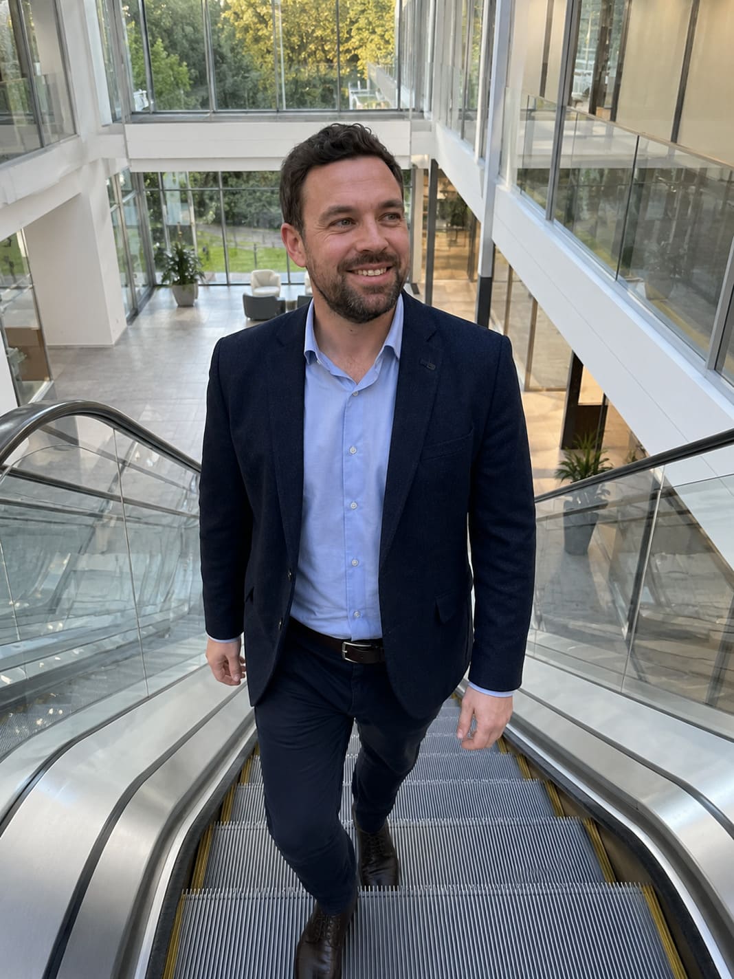 FM ascending an escalator inside a modern glass-fronted office building