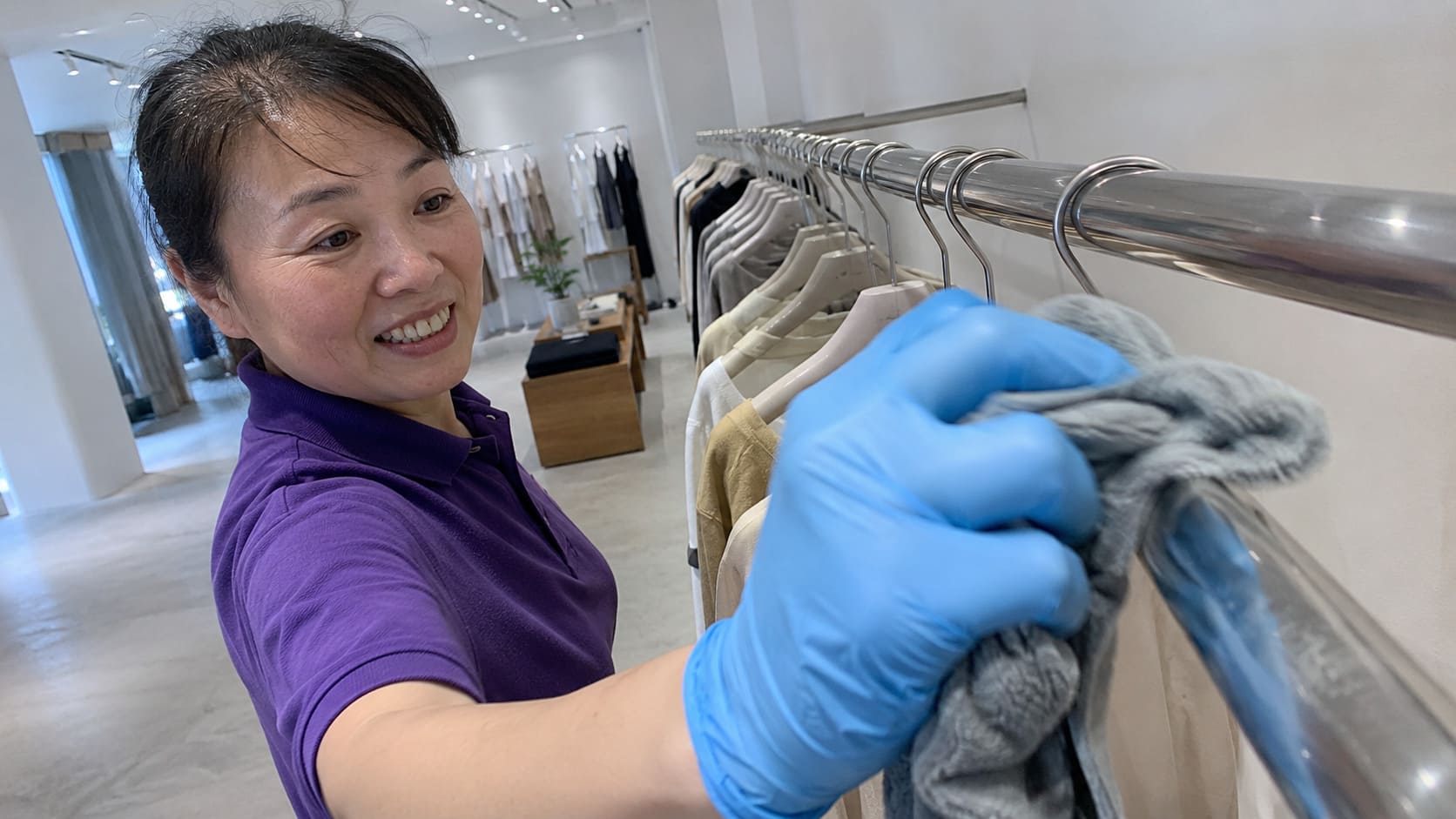 Cleaner polishing a chrome clothing rail in a minimalist fashion boutique