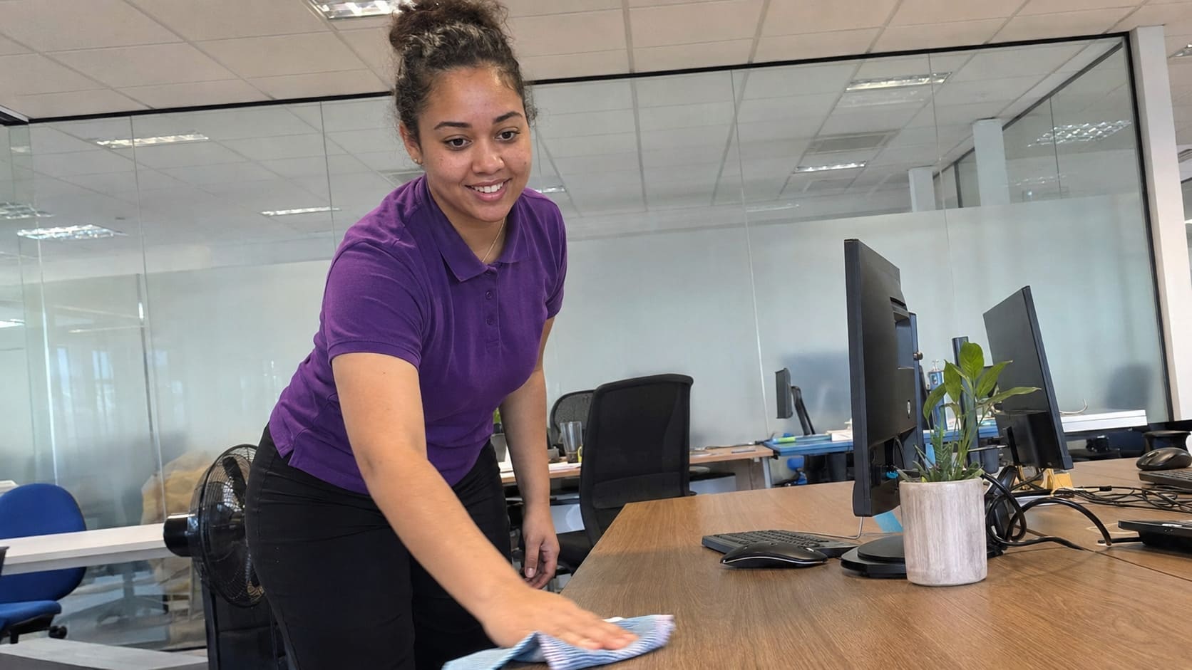 Cleaner wiping a workstation desk in a glass-partitioned office