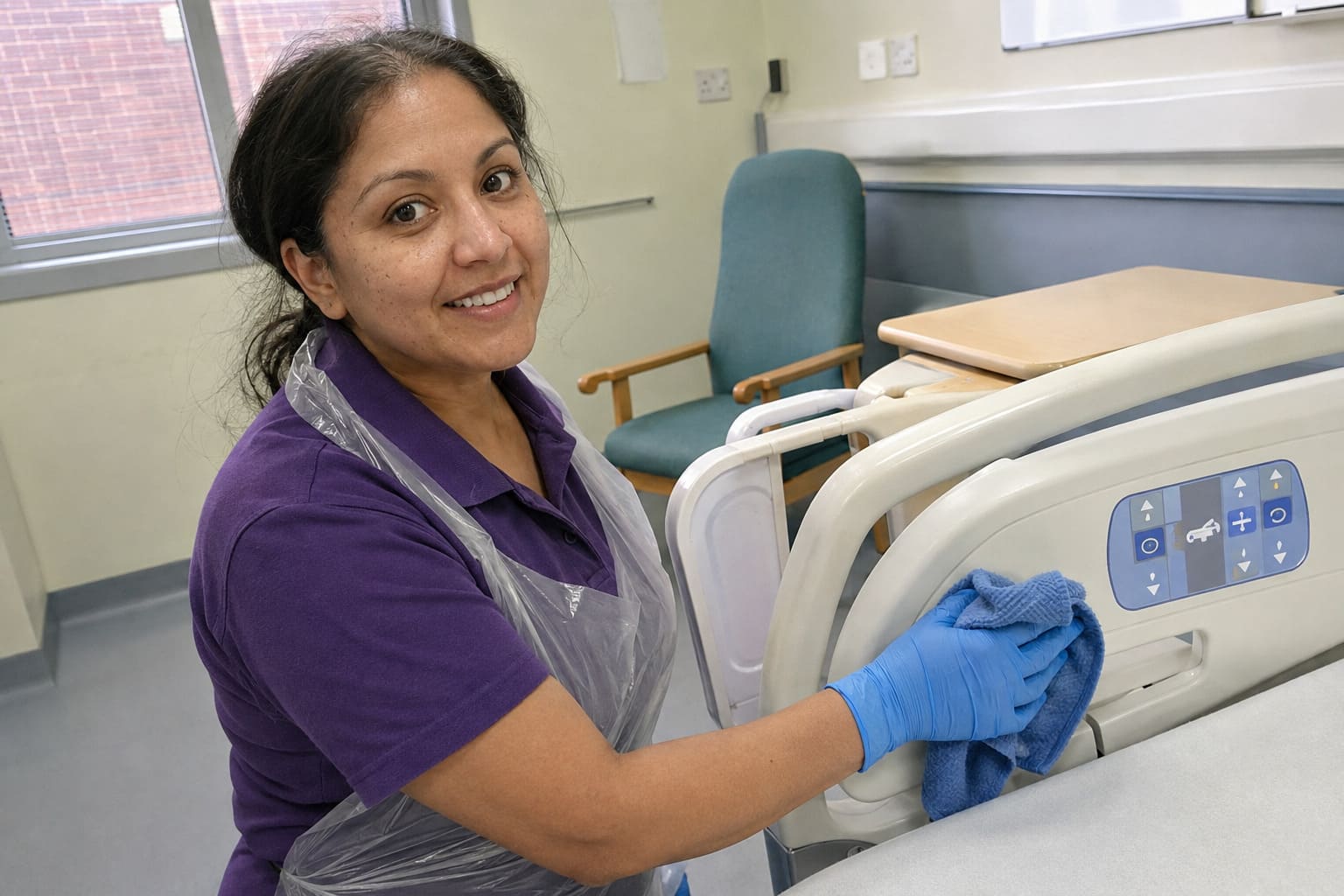 Healthcare cleaner disinfecting hospital bed controls during clinical cleaning - Illustrative Image