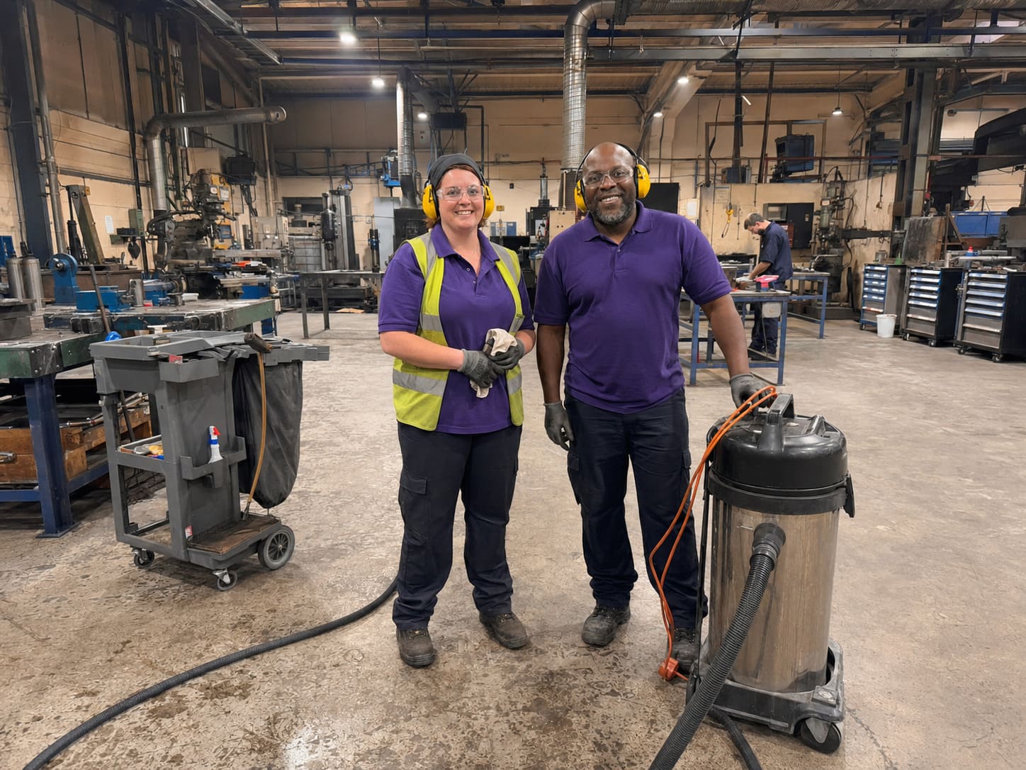 Industrial cleaning team with vacuum equipment inside engineering workshop