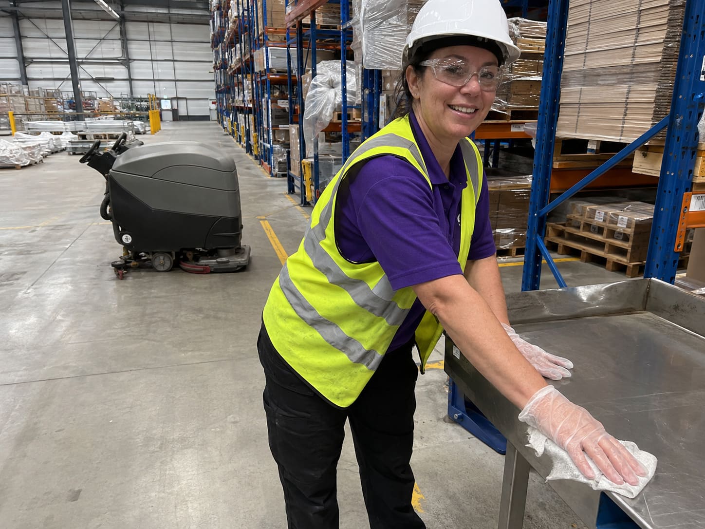 Warehouse worker cleaning floors beside storage racking